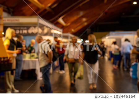 Dark blurry shot of people at the exhibition. People walk around, try different things and shop. 108446164