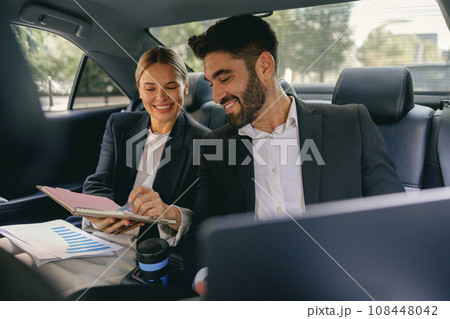 Smiling business analysts have online meeting using laptop while sitting in car back seats 108448042