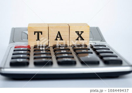 Tax word on wooden cubes on top of a calculator with white background. Tax and financial concept. Tax word on wooden cubes on top of a calculator with white background. Tax and financial concept. 108449437