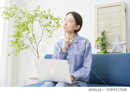 リビングでパジャマ姿でノートパソコンを使いながら考える女性 リビングでパジャマ姿でノートパソコンを使いながら考える女性 108451566