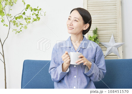 リビングでパジャマ姿で温かい飲み物を飲む女性 108451570