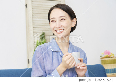 リビングでパジャマ姿で温かい飲み物を飲む女性 リビングでパジャマ姿で温かい飲み物を飲む女性 108451571