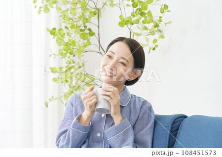 リビングでパジャマ姿で温かい飲み物を飲む女性 108451573