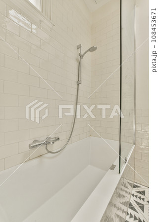 a white bathtub in a bathroom with tiled walls and black and white tiles on the floor, there is a glass shower door 108453671