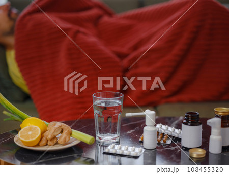 Ginger, lemon, onion and different drugs on table on background sick man. Alternative remedies and traditional pills to treat colds and flu. Natural medicine vs conventional medicine concept Ginger, lemon, onion and different drugs on table on background sick man. Alternative remedies and traditional pills to treat colds and flu. Natural medicine vs conventional medicine concept 108455320