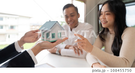 Young married couple sitting at table listening to realtor, real estate agent, loan broker or mortgage advisor telling about options 108455750