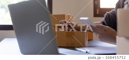 Woman is writing a list of customer on box before shipping to them, she runs an ecommerce business on websites and social media. Concept of selling products online 108455752