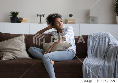 Happy thoughtful young black woman, African girl relaxing on couch Happy thoughtful young black woman, African girl relaxing on couch 108462139
