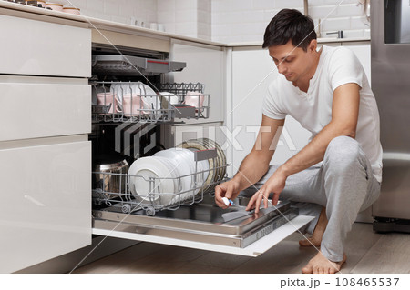 handsome man putting detergent tablet into dishwasher in kitchen 108465537