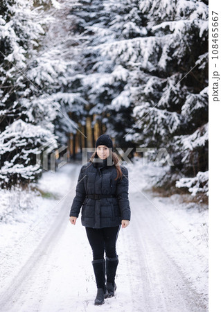 Beautiful girl in black winter clothes walking in snowy forest. Christmas Hollidays  108465667