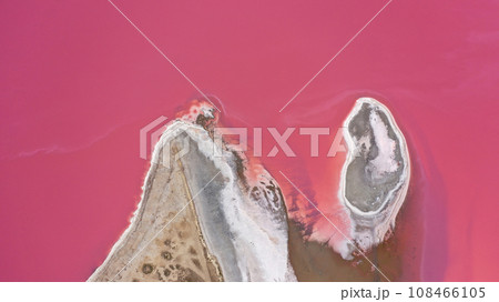Flying over a pink salt lake. Salt production facilities saline evaporation pond fields in the salty lake. Dunaliella salina impart a red, pink water in mineral lake with dry cristallized salty coast. Flying over a pink salt lake. Salt production facilities saline evaporation pond fields in the salty lake. Dunaliella salina impart a red, pink water in mineral lake with dry cristallized salty coast. 108466105