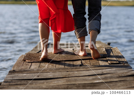 Cropped photo young lovers married couple, husband and wife, held of hands on a wooden bridge near lake. Rear view of couple standing on pier. lower half. Place for text and design. Close Up. Cropped photo young lovers married couple, husband and wife, held of hands on a wooden bridge near lake. Rear view of couple standing on pier. lower half. Place for text and design. Close Up. 108466113