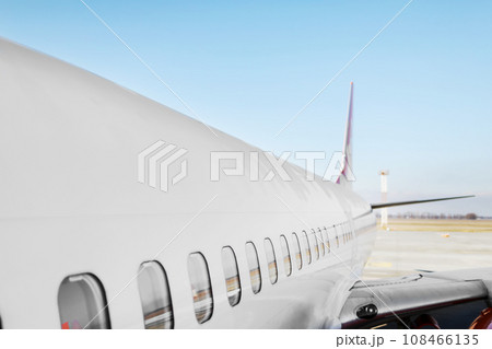 Aircraft porthole - side window airplain. White heavy passenger jet engine airplane on runway at airport against blue sky aviation transportation theme background. Aircraft porthole - side window airplain. White heavy passenger jet engine airplane on runway at airport against blue sky aviation transportation theme background. 108466135