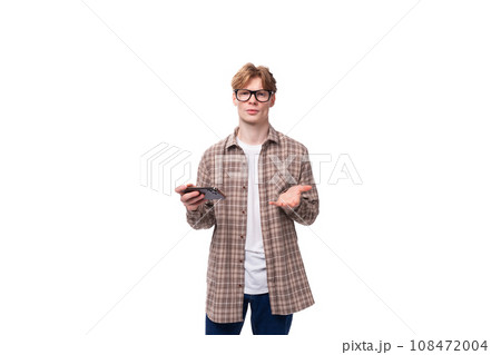 a young european man with red short hair and glasses is dressed in a plaid shirt holding a phone in 108472004