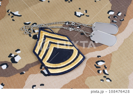 US ARMY Sergeant First Class rank patch and dog tags on Desert Battle Dress Uniform background US ARMY Sergeant First Class rank patch and dog tags on Desert Battle Dress Uniform background 108476428