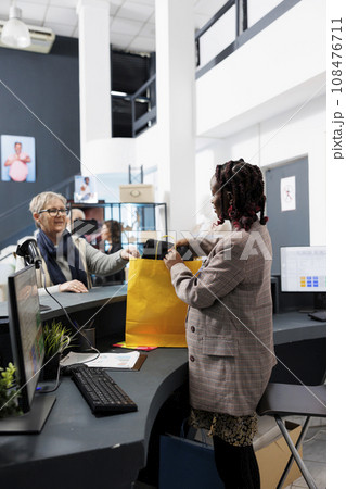 African american employee preparing bag with purchase for elderly client in modern boutique. Fashionable woman buying stylish casual wear in store, making electronic payment at pos terminal. 108476711