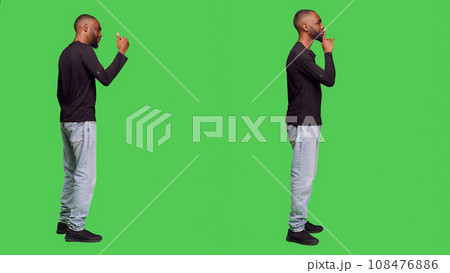 Confident man doing silence mute sign and calling over someone to join, showing privacy in studio. Young person showing hush gesture to keepy secret, raising hand and saying come over. Confident man doing silence mute sign and calling over someone to join, showing privacy in studio. Young person showing hush gesture to keepy secret, raising hand and saying come over. 108476886