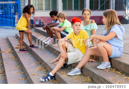 Positive tweenagers friendly blabbing while sitting on steps outdoors 108478953