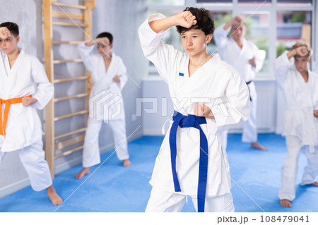 Teenager in kimono practicing punches during group martial arts workout 108479041