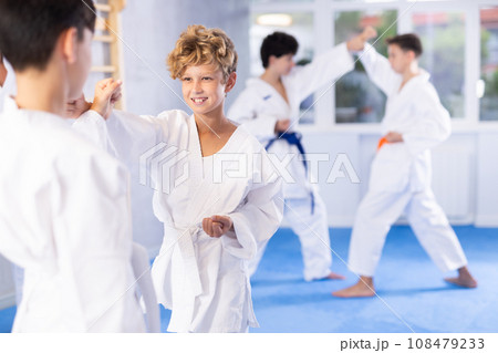 Diligent preteen attendee of karate classes fighting with his opponent in sports hall Diligent preteen attendee of karate classes fighting with his opponent in sports hall 108479233