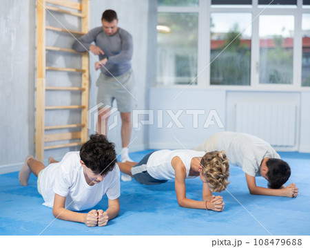 Focused teen boys doing forearm plank during workout at gym Focused teen boys doing forearm plank during workout at gym 108479688