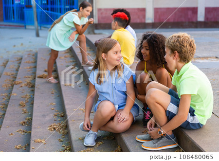 Children talking together while sitting on stairs outdoors Children talking together while sitting on stairs outdoors 108480065