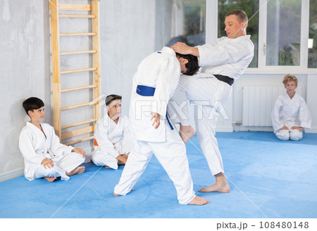 Instructor demonstrating karate techniques to group of teenagers in sparring with boy Instructor demonstrating karate techniques to group of teenagers in sparring with boy 108480148