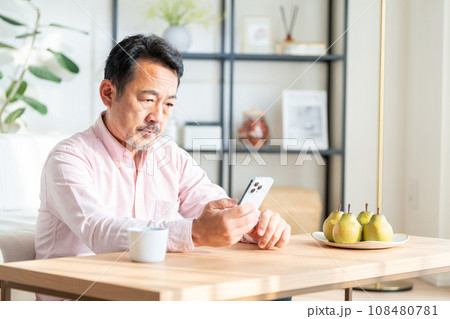 リビングでスマートフォンを操作するシニア男性。 リビングでスマートフォンを操作するシニア男性。 108480781