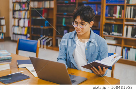 Male college students are working on laptops and searching for books to study, make reports, find useful information in college room. Concept of reading, learning and intelligence. Male college students are working on laptops and searching for books to study, make reports, find useful information in college room. Concept of reading, learning and intelligence. 108481958