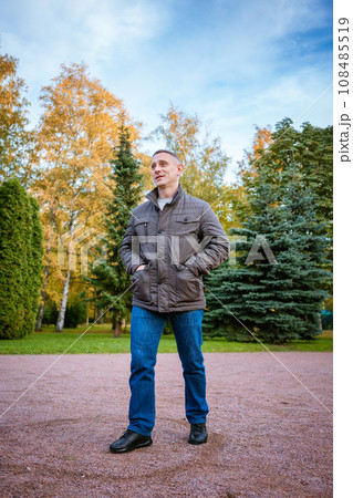 a man in an autumn jacket in the park stands on the path 108485519