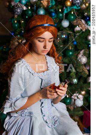 young woman in a beautiful dress sits near the Christmas tree 108485957