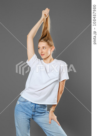 Blonde woman wearing blue jeans and white shirt playing with her long hair Blonde woman wearing blue jeans and white shirt playing with her long hair 108487980