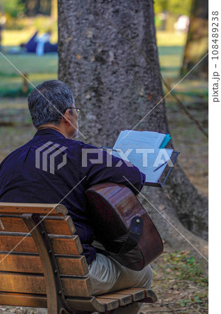 公園の公園のベンチに座りギターの練習をする男性 108489238
