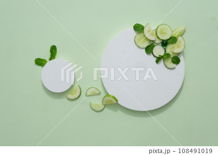 Empty cylindrical platform for cosmetics with cucumber ingredient. Mockup with concrete circle decorated with cucumber slices and mint leaves on green background Empty cylindrical platform for cosmetics with cucumber ingredient. Mockup with concrete circle decorated with cucumber slices and mint leaves on green background 108491019
