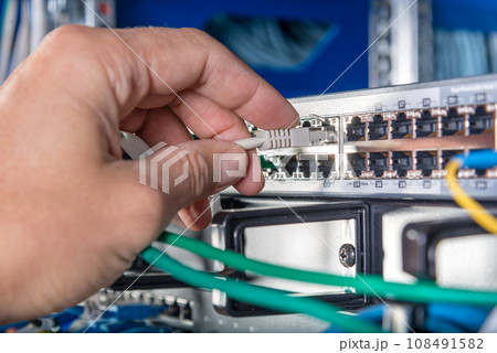 closeup of hand of administrator connecting network cable into switch closeup of hand of administrator connecting network cable into switch 108491582