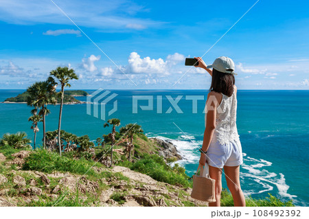Traveler asian woman with mobile phone travel on summer beach at Promthep cape Phuket Thailand Traveler asian woman with mobile phone travel on summer beach at Promthep cape Phuket Thailand 108492392