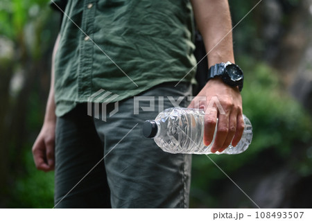 Male hiker holding water bottle against background of green tropical forest Male hiker holding water bottle against background of green tropical forest 108493507