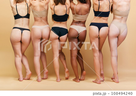 Back view of female bodies of different shapes and skin color standing in underwear against beige studio background. Buttocks and legs Back view of female bodies of different shapes and skin color standing in underwear against beige studio background. Buttocks and legs 108494240