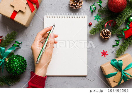 Woman writing Christmas to do list on notebook on colored background with xmas decorations 108494595
