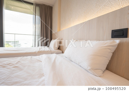 2 single beds with white bedding are in the cream bedroom of hotel that turn on the headboard light and open the gray curtain. 2 single beds with white bedding are in the cream bedroom of hotel that turn on the headboard light and open the gray curtain. 108495520