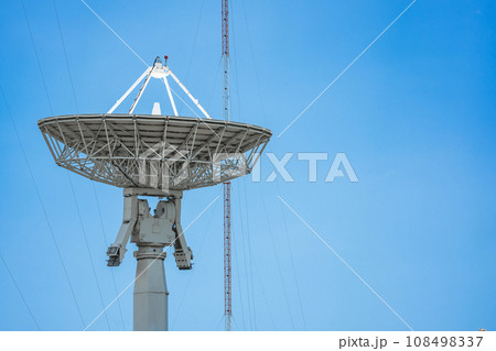 parabolic antenna satellite dish located in front of telecommunication tower with a clear blue sky in the background. 108498337