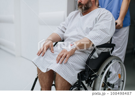Male nurse pushing a patient in a wheelchair along a hospital corridor, waiting for medical examination. Overweight patient feeling anxious and has health concerns. 108498487