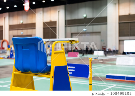 Blue chair of badminton referee with yellow colors near badminton net with blurred background in sport indoor stadium. Blue chair of badminton referee with yellow colors near badminton net with blurred background in sport indoor stadium. 108499103