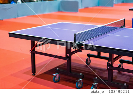 Blue table tennis or pingpong table is settle on a red, orange floor of the indoor court stadium for competitions tournament. 108499211