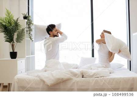 Young passionate Caucasian couple fighting with pillows Young passionate Caucasian couple fighting with pillows 108499536