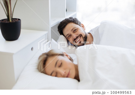 Man smiling on camera while woman sleeping in bed 108499563