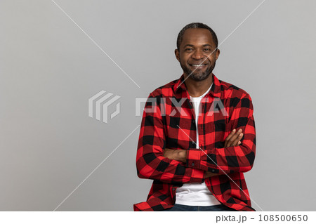 Smiling black bearded man wearing red checkered shirt keeps hands folded Smiling black bearded man wearing red checkered shirt keeps hands folded 108500650