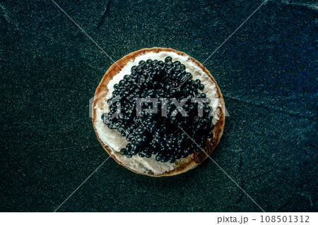 A blini with caviar and cream cheese, overhead flat lay shot on black 108501312