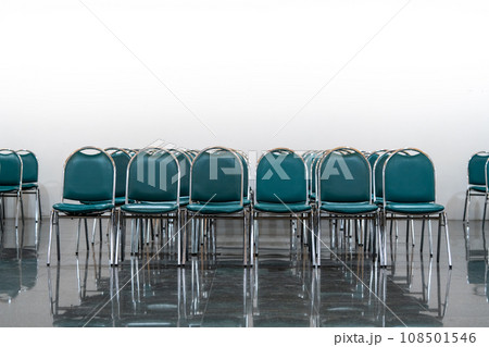 Many empty green leather chairs in a wide hall room, lights on. A floor reflect the objects. Give a feeling of emptiness. Many empty green leather chairs in a wide hall room, lights on. A floor reflect the objects. Give a feeling of emptiness. 108501546