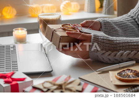 Female buyer makes order on laptop. Woman picking gifts online purchases at cozy home among gift boxes and packages. Winter sales, Black Friday. Christmas discount promotions. Blurred bokeh light. Female buyer makes order on laptop. Woman picking gifts online purchases at cozy home among gift boxes and packages. Winter sales, Black Friday. Christmas discount promotions. Blurred bokeh light. 108501684